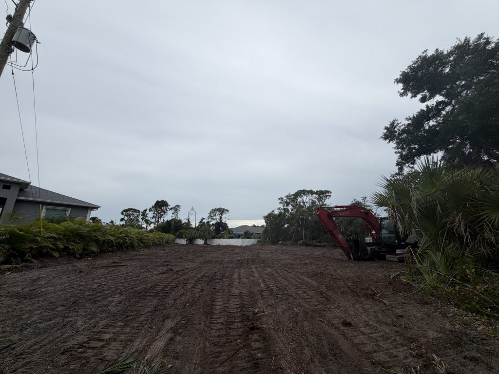 Graded residential lot with excavator and retained trees along the boundary