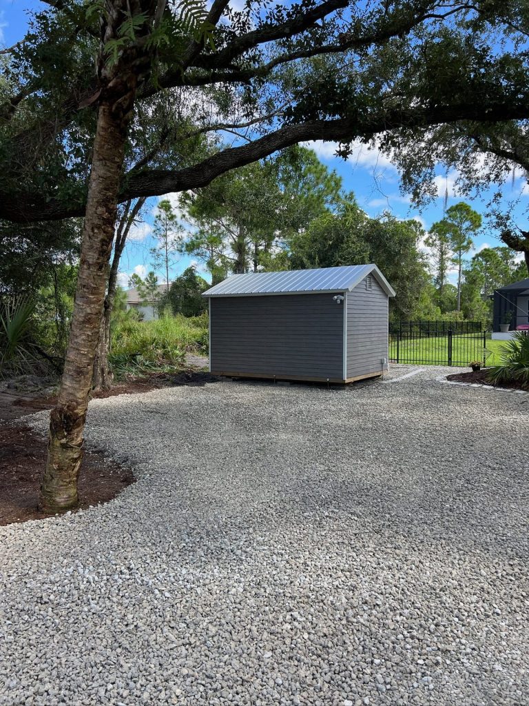 Decorative rock pad leading to a backyard shed under an oak tree