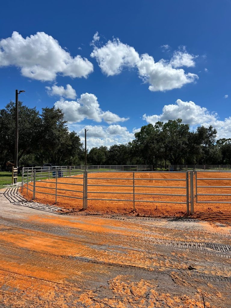 Round horse arena with red clay footing and pipe-rail fence built by Liberty Services in Southwest Florida
