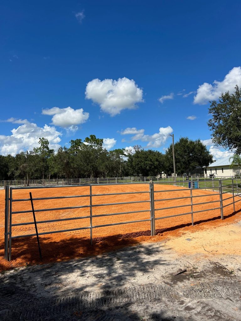 Pipe-rail arena fence and freshly graded red clay footing on a new horse arena
