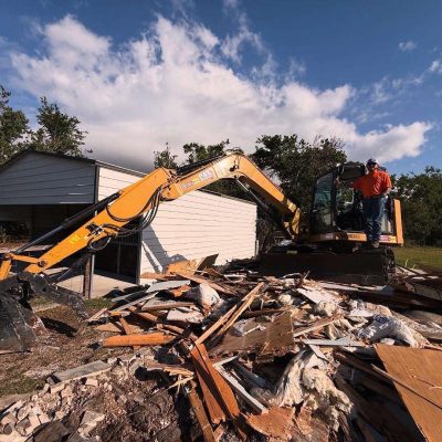 Yellow excavator on top of recently demo yellow barn.