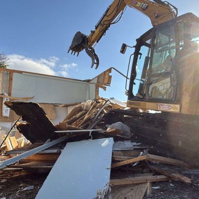 Yellow excavator used to demolition a yellow barn.