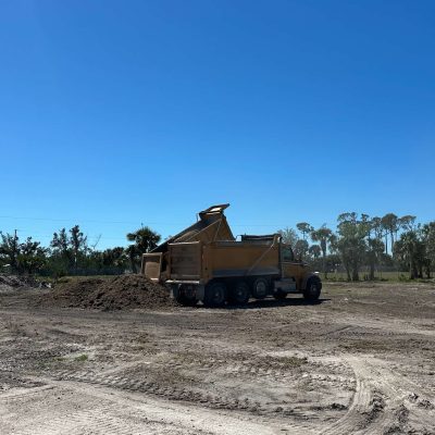 Yellow dump truck dropping off soil for site grading project.